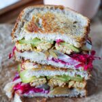 Straight on, close-up view of a tempeh reuben sandwich, sliced in half and stacked to show the sandwich filling.