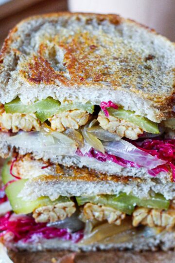 Straight on, close-up view of a tempeh reuben sandwich, sliced in half and stacked to show the sandwich filling.