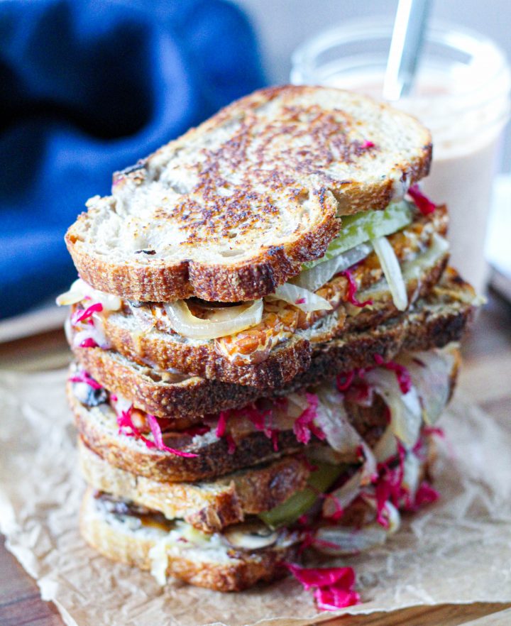 a straight on shot of a stack of 3 tempeh Reubens on a wooden serving board