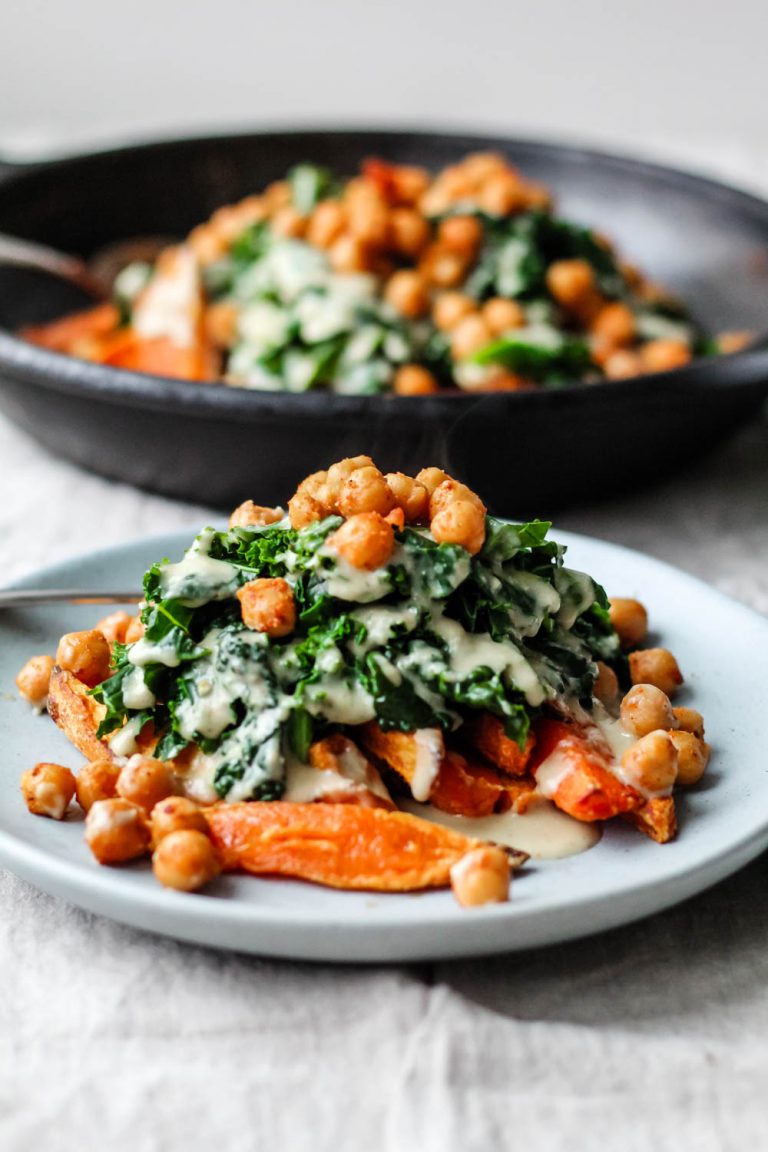 straight on shot of the sweet potato fries on a blue plate loaded with the gravy, kale, and chickpeas.