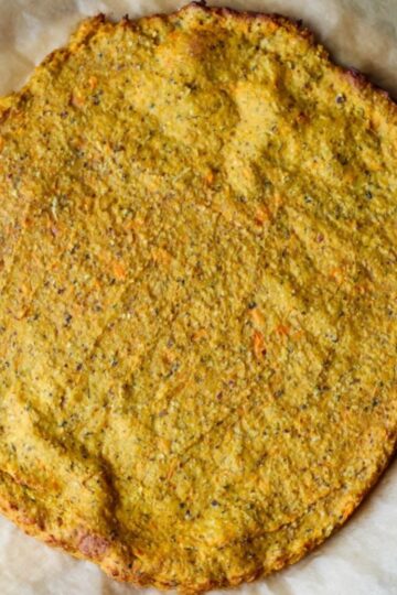 An overhead photo of the sweet potato oat flour pizza crust on a sheet of parchment, freshly baked