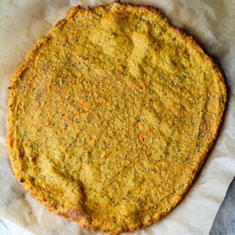 An overhead photo of the sweet potato oat flour pizza crust on a sheet of parchment, freshly baked