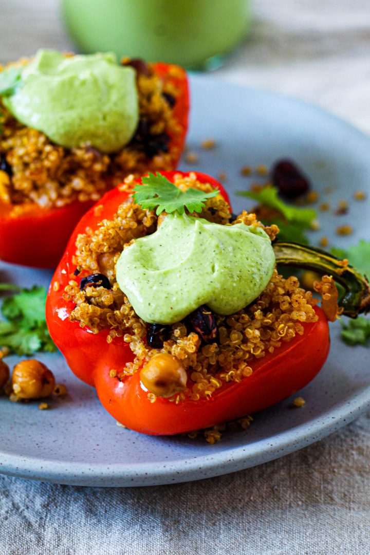 straight on shot of the stuffed peppers on a blue plate topped with cilantro avocado sauce