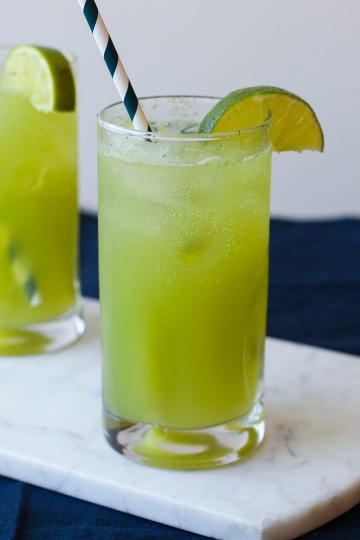 straight on shot of cucumber mint limeade with a striped paper straw in it on a white marble board 