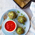 overhead shot of three rice balls on a blue plate with marinara sauce in a dish