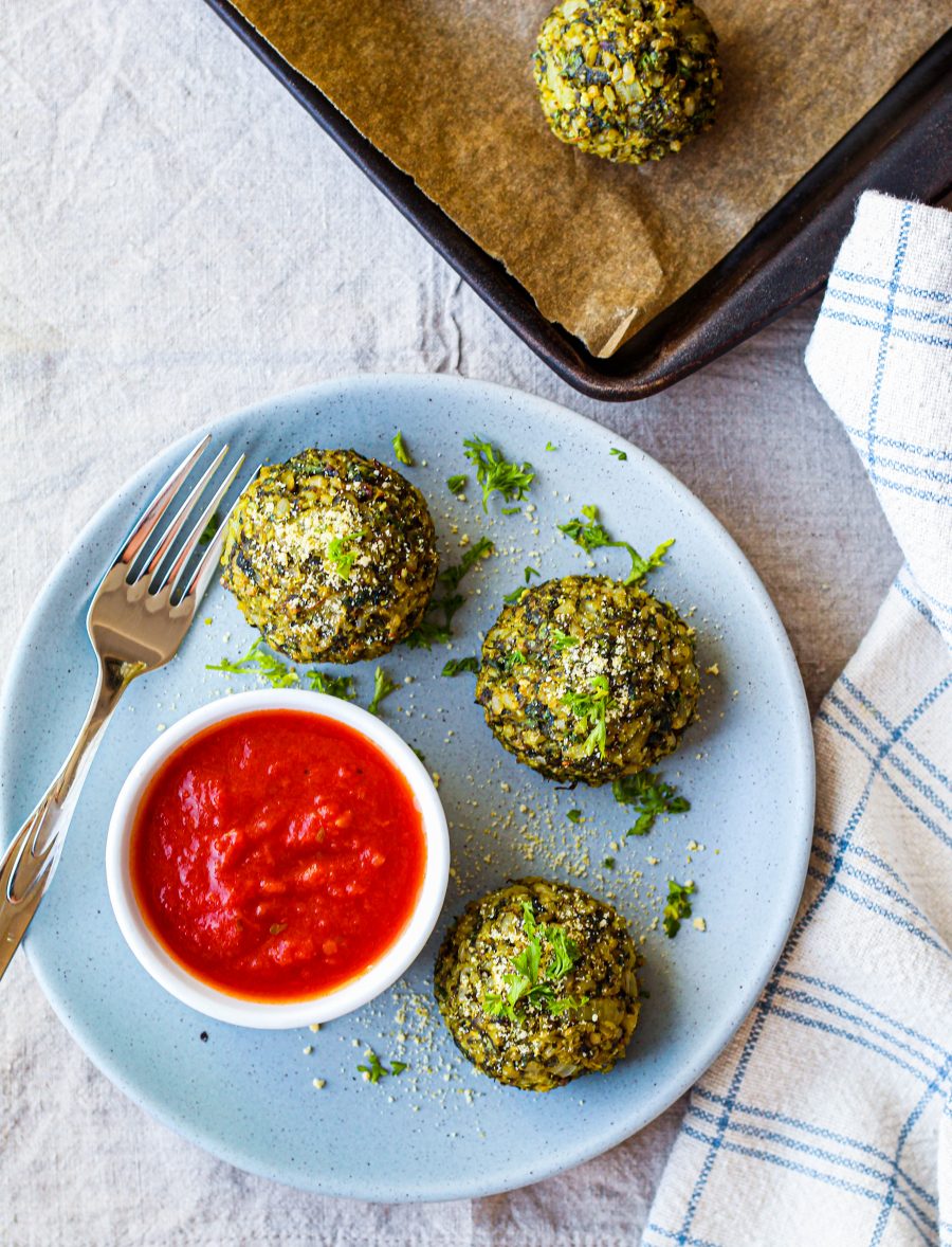 overhead shot of three rice balls on a blue plate with marinara sauce in a dish