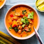 overhead photo of a bowl of peanut, chickpea, and sweet potato soup in a light pink bowl against a blue backdrop
