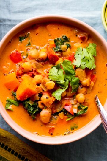 overhead photo of a bowl of peanut, chickpea, and sweet potato soup in a light pink bowl against a blue backdrop
