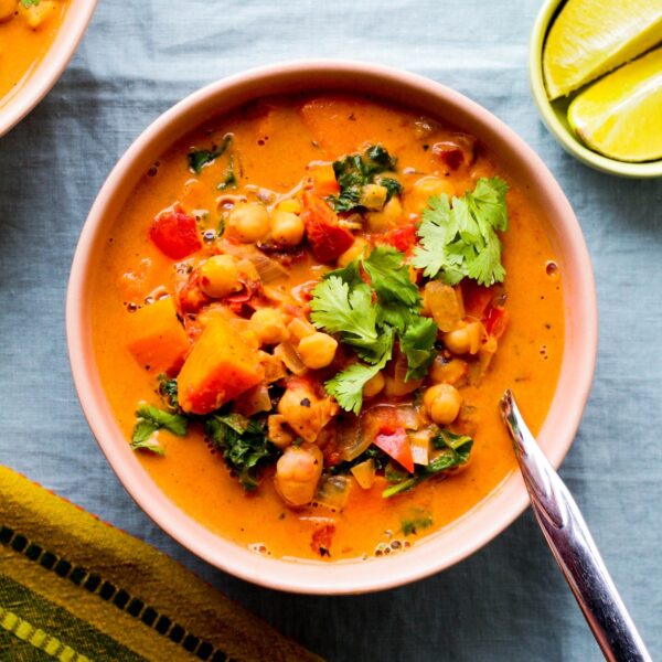 overhead photo of a bowl of peanut, chickpea, and sweet potato soup in a light pink bowl against a blue backdrop