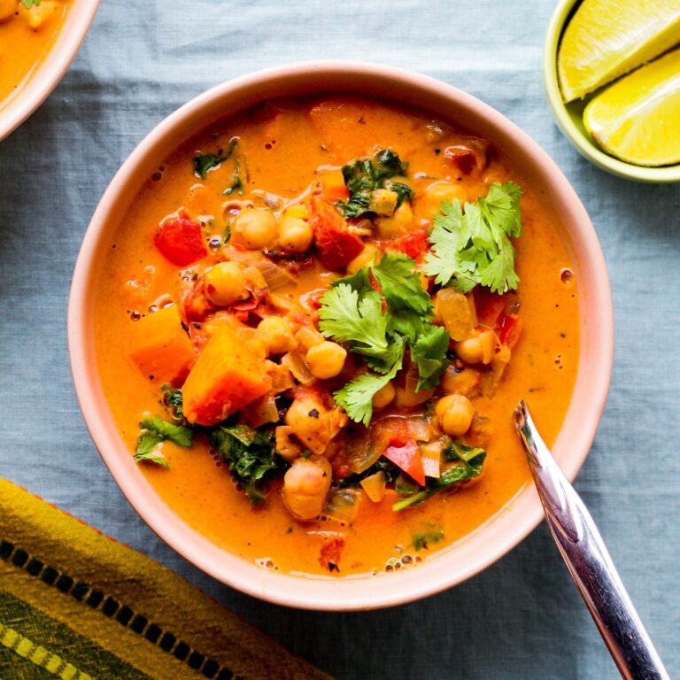 overhead photo of a bowl of peanut, chickpea, and sweet potato soup in a light pink bowl against a blue backdrop