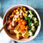 overhead shot of a bowl with roasted potato, beets, carrots, and steamed kale, roasted chickpeas, and nutritional yeast dressing drizzled over top