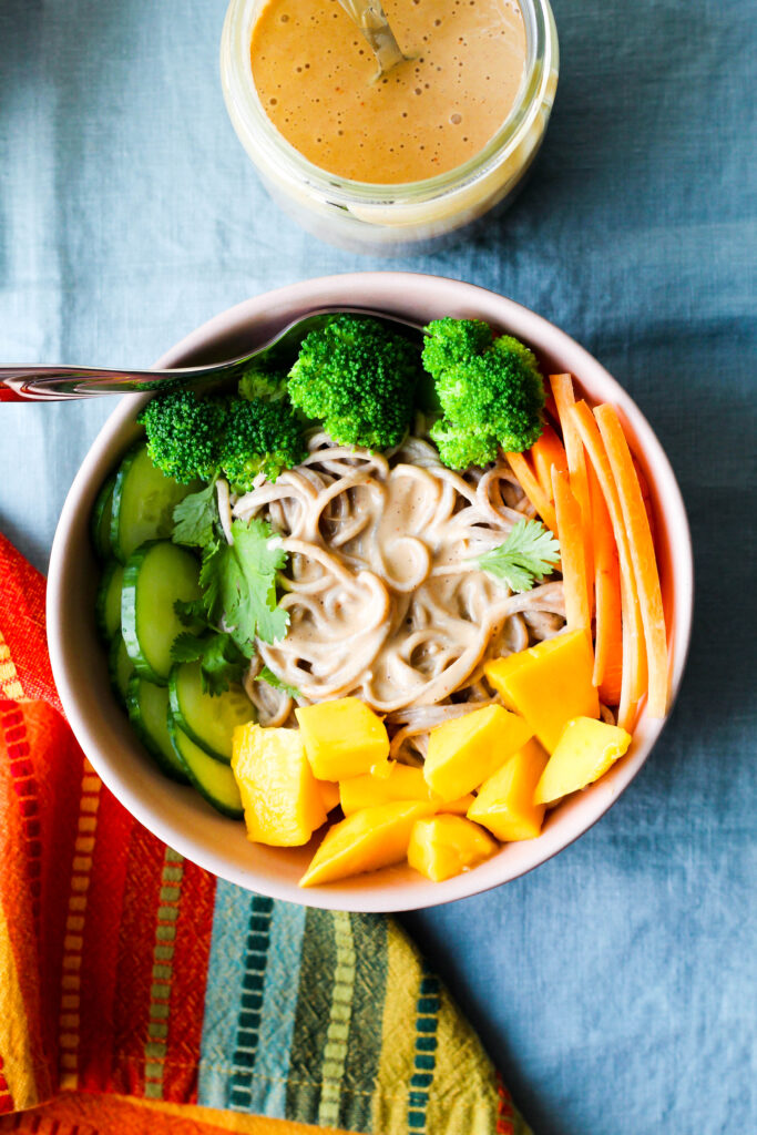 overhead shot of one bowl of peanut butter noodles garnished with carrots, mango, and broccoli 