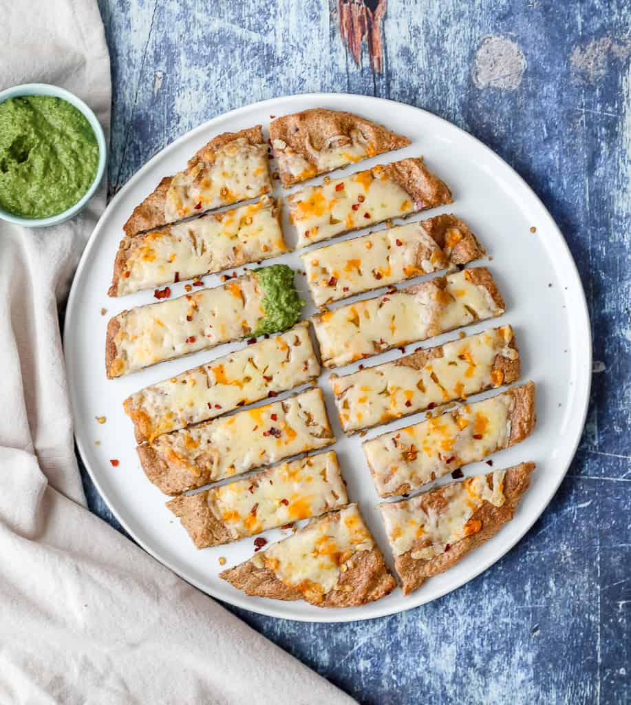 an overhead shot of buckwheat pizza crust cheese bread sliced into small pieces on a blue backdrop 