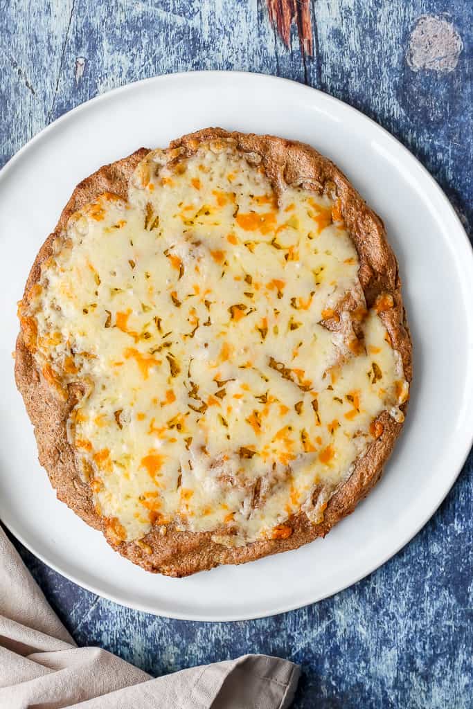 overhead shot of the pizza crust topped with melted cheese on a white plate 