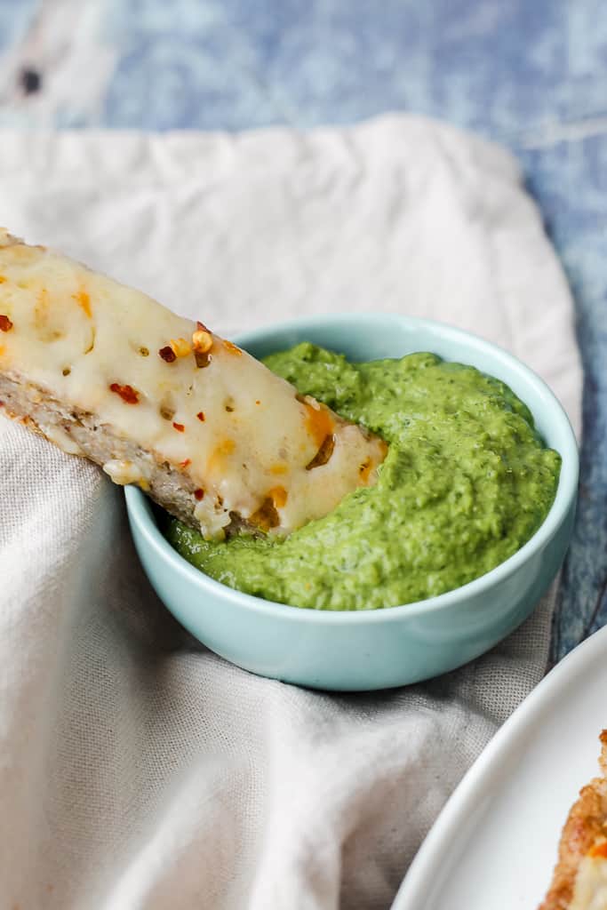 a photo of a piece of buckwheat pizza crust cheese bread being dipped into a dish of pesto 