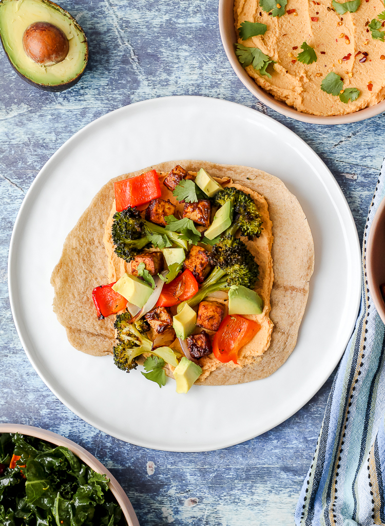 a zoomed out overhead shot of a wrap on a white plate with hummus and avocado around it