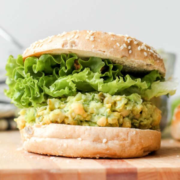 straight on view of a sandwich with smashed chickpeas, avocado, and dill pickles on a wooden board