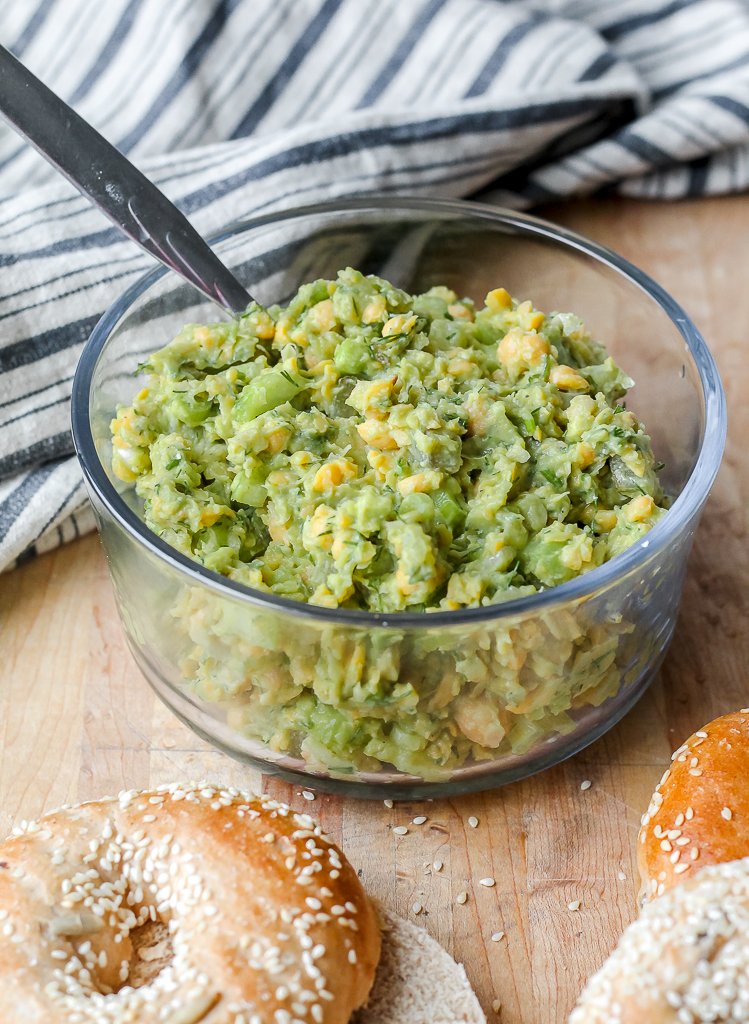 straight on shot of a container of the smashed chickpea avocado salad on a wooden board 