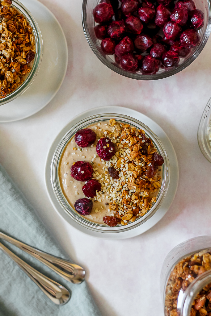 an overhead photo of a bowl of quinoa peanut butter banana breakfast pudding in a glass dish topped with cherries and granola