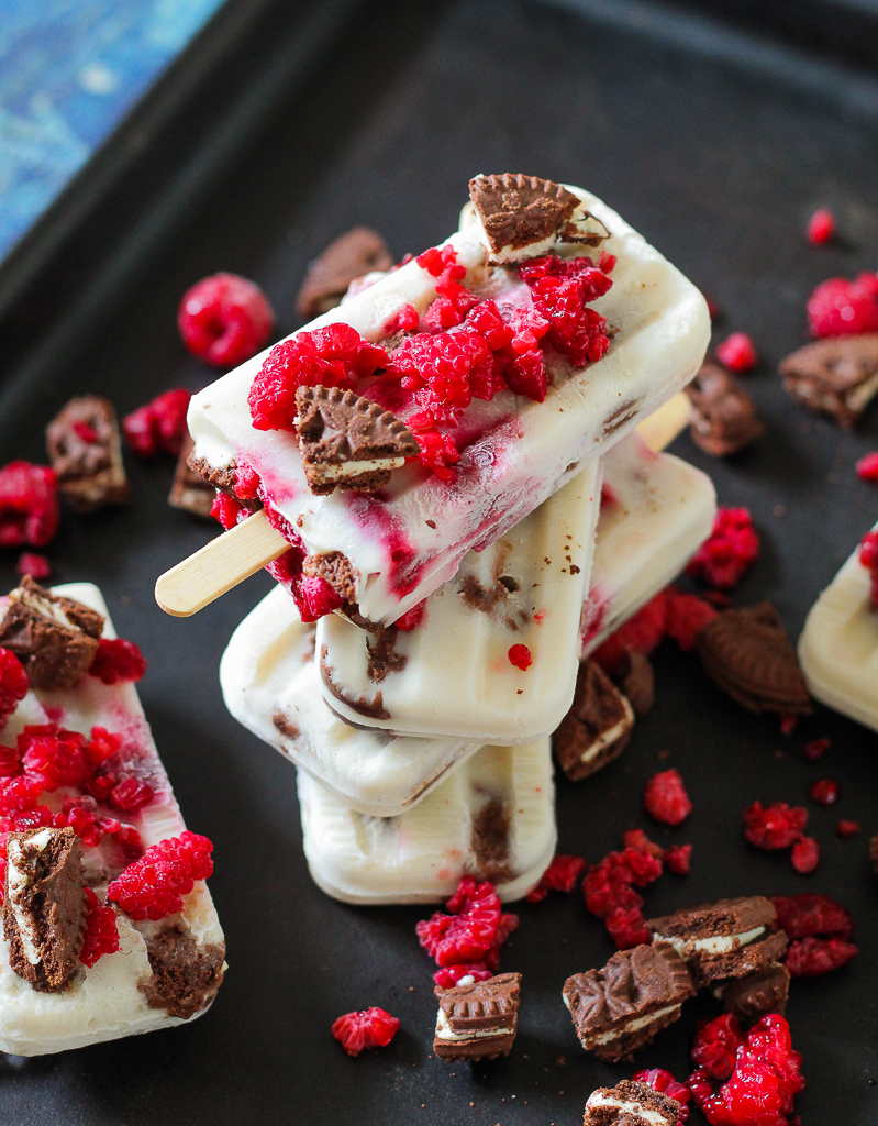 a stack of four cookies and cream raspberry popsicles on a dark cookie sheet 