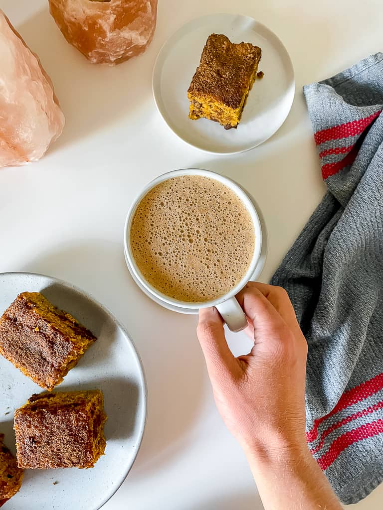 an overhead photo of the pumpkin chai hot chocolate in a mug on a white table surrounded by pieces of pumpkin cake on plates