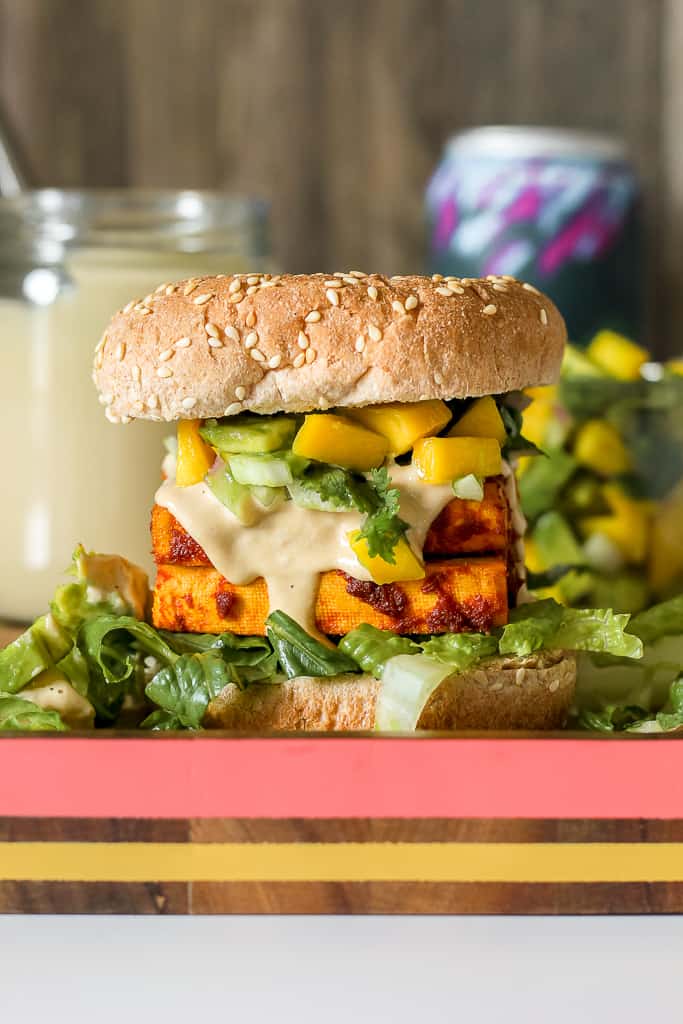 straight on photo of the red curry tofu sandwich with a jar of tahini sauce and mango salsa in the background