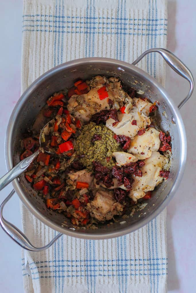 overhead process shot showing the chicken, veggies, and pesto in a pot