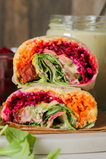 close up straight on view of a wrap with tofu, colourful shredded carrots and beets, caesar dressing, avocado, and arugula.