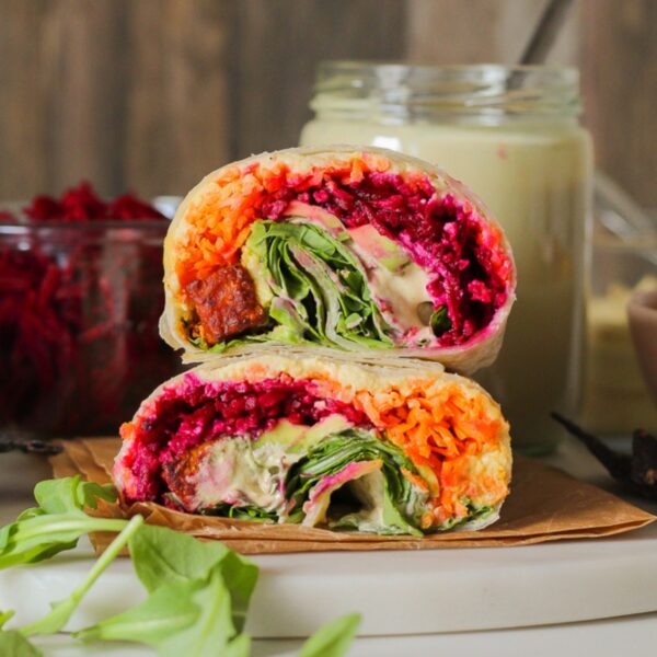 close up straight on view of a wrap with tofu, colourful shredded carrots and beets, caesar dressing, avocado, and arugula.