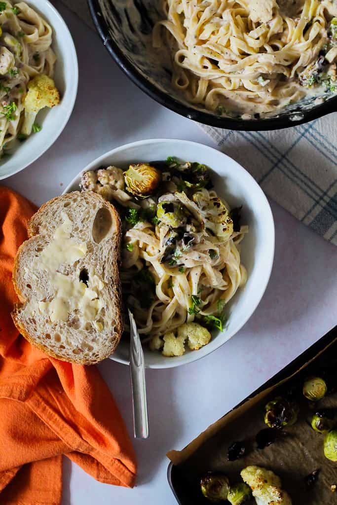 a bowl of pasta with a slice of bread and butter on a light pink surface