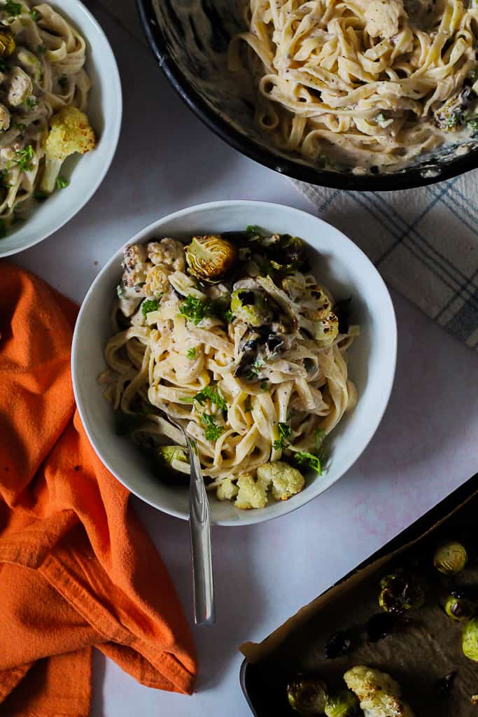 overhead shot of a serving of pasta in a white bowl surrounded by the skillet and the cookie sheet of roasted vegetables