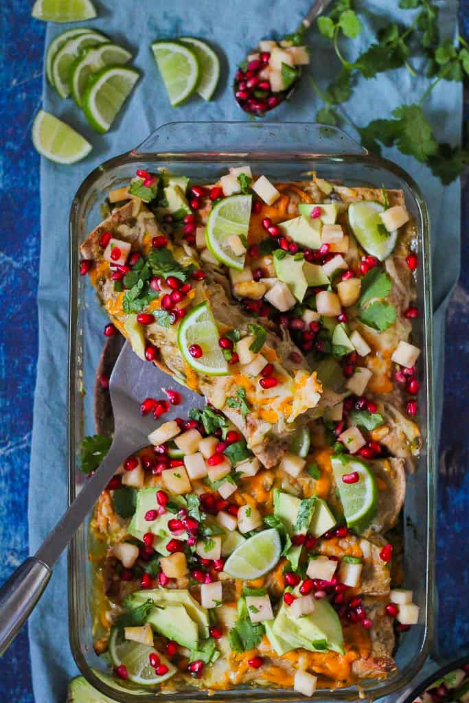 overhead shot of one enchilada on a spatula about to be dished out of the pan on a blue background