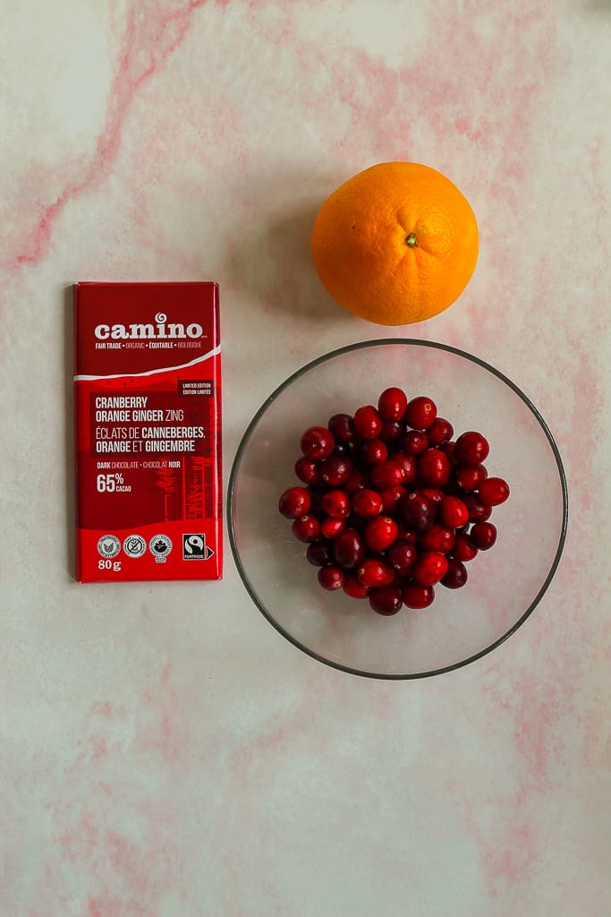 overhead shot of a bowl of the cranberries, orange, and cranberry orange chocolate bar on a light pink backdrop