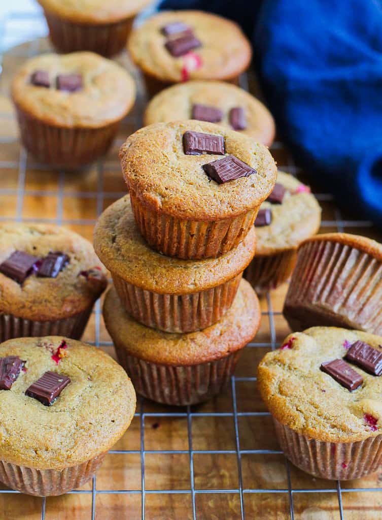 a straight on shot of a stack of three cranberry orange chocolate chunk muffins on a wire rack with other muffins arranged around it