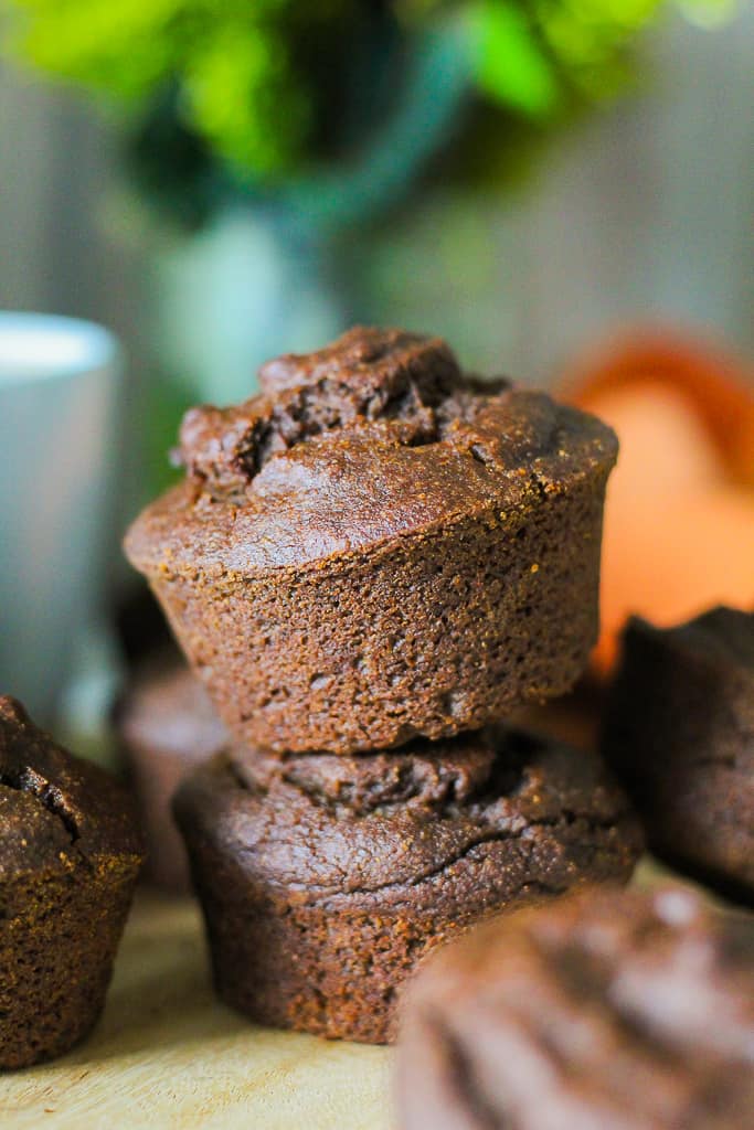 straight on shot of the pumpkin gingerbread muffins, two stacked on a wooden board with a vase of flowers in behind.