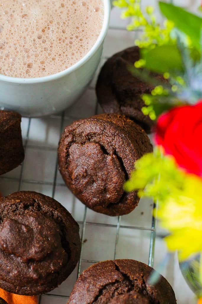 angled shot of the pumpkin gingerbread muffins on a wire rack against a mug of hot cocoa