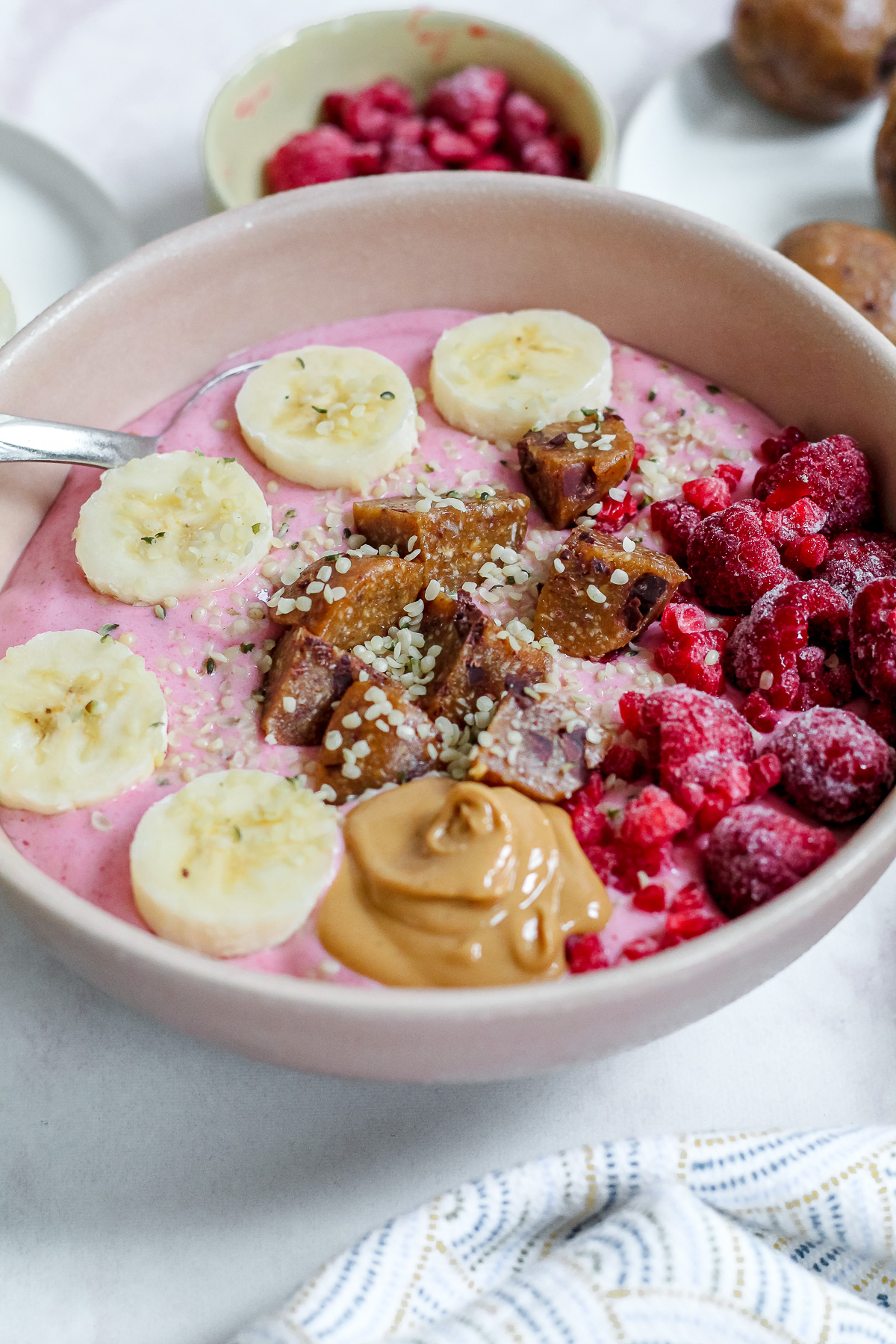 angled close up straight on shot of a raspberry smoothie bowl with a dish of raspberries and some energy balls in the background