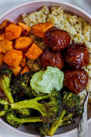 overhead photo of a bowl of bbq meatballs, roasted broccoli and sweet potato, quinoa, and avocado sauce