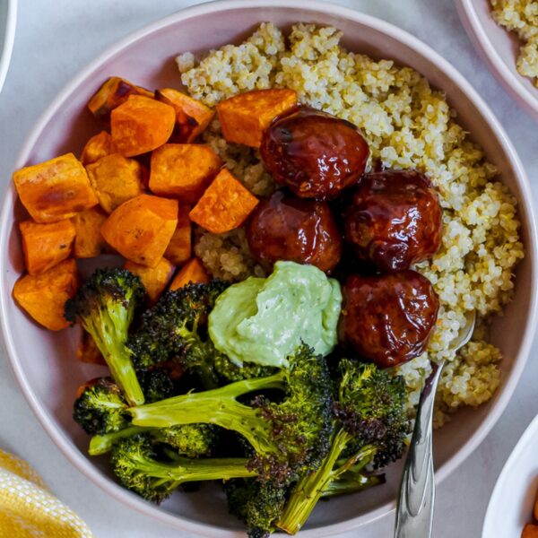 overhead photo of a bowl of bbq meatballs, roasted broccoli and sweet potato, quinoa, and avocado sauce