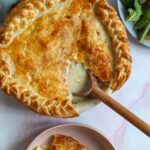 overhead photo of the chicken sausage pot pie in a large pie plate with a serving of it in a bowl against a bright backdrop