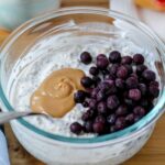 featured image for the post: photo of a container of overnight oats topped with peanut butter and blueberries on a wooden table
