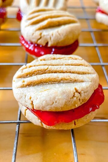 featured image, a close up photo of a peanut butter and jam sandwich cookie on a wire rack