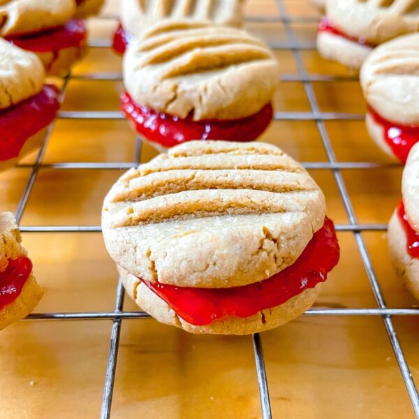 featured image, a close up photo of a peanut butter and jam sandwich cookie on a wire rack