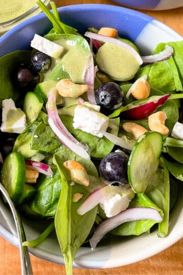 an overhead photo of a serving of the salad with blueberries, spinach, feta, cashews, and lemon mint dressing.
