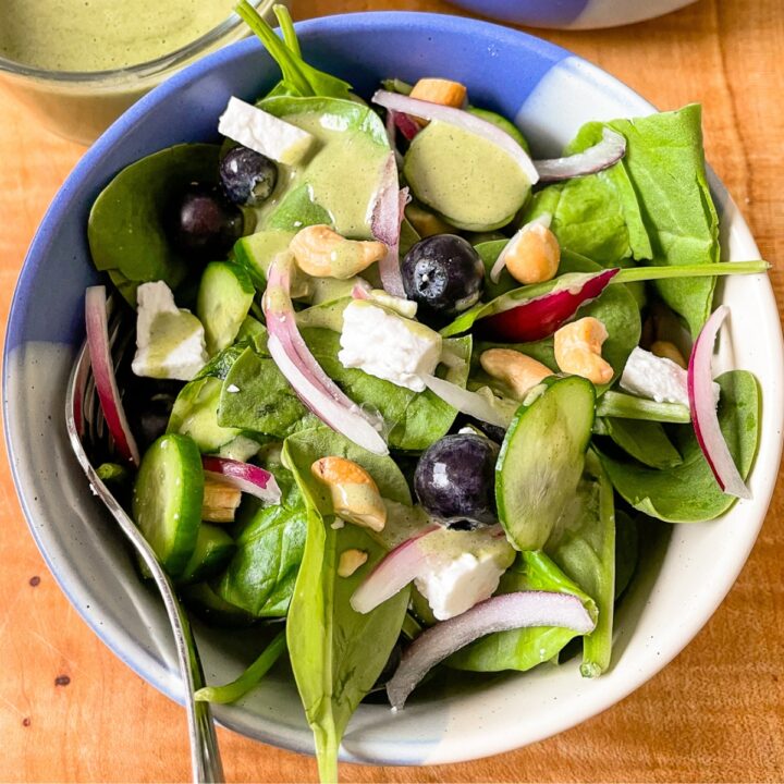 an overhead photo of a serving of the salad with blueberries, spinach, feta, cashews, and lemon mint dressing.