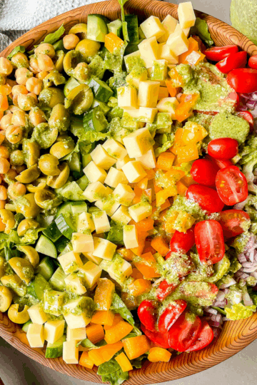 overhead photo of the salad in a large wooden bowl with pesto dressing drizzled over top