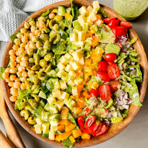 overhead photo of the salad in a large wooden bowl with pesto dressing drizzled over top