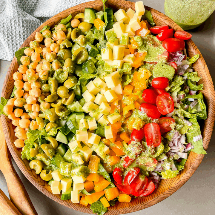 overhead photo of the salad in a large wooden bowl with pesto dressing drizzled over top
