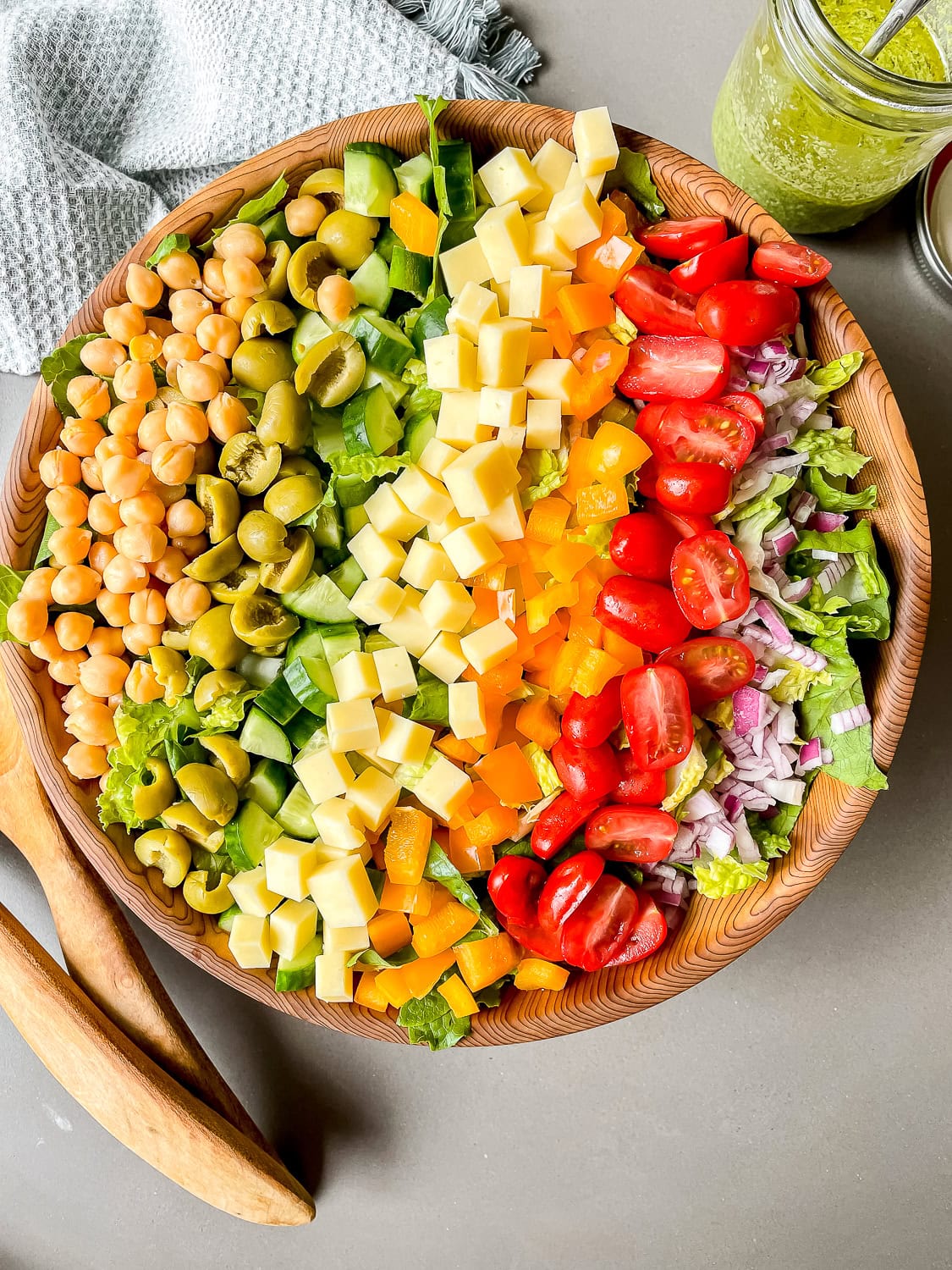 a process photo of the fully assembled salad in a large wooden bowl with a jar of dressing in the upper right hand corner