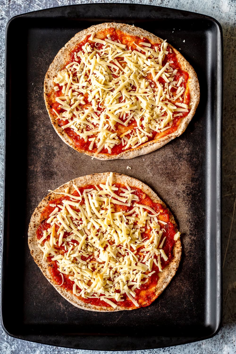 a process photo showing two pitas with pizza sauce and shredded cheese